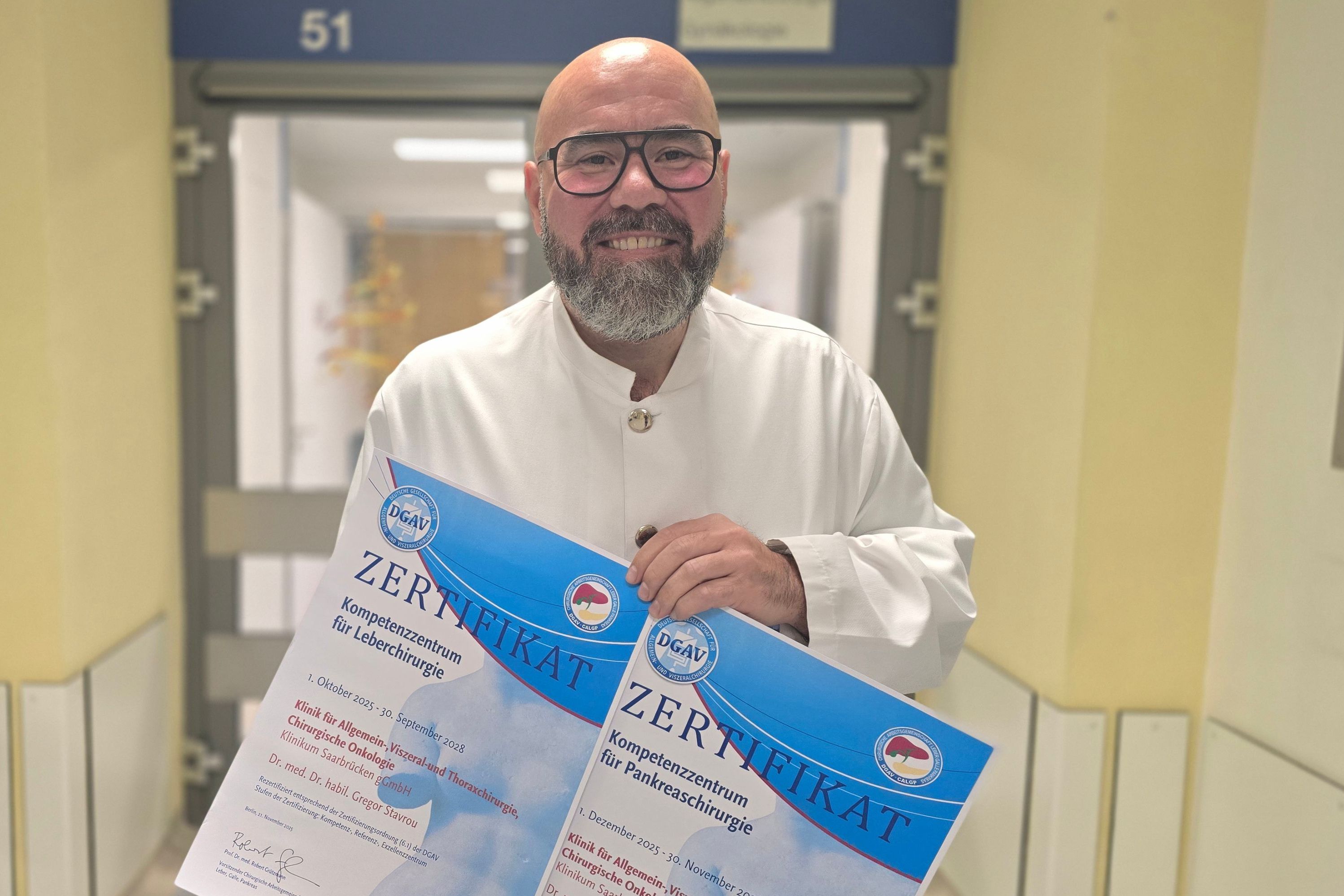 Chefarzt Dr. Dr. habil Gregor Stavrou zeigt die beiden neuen Zertifikate.