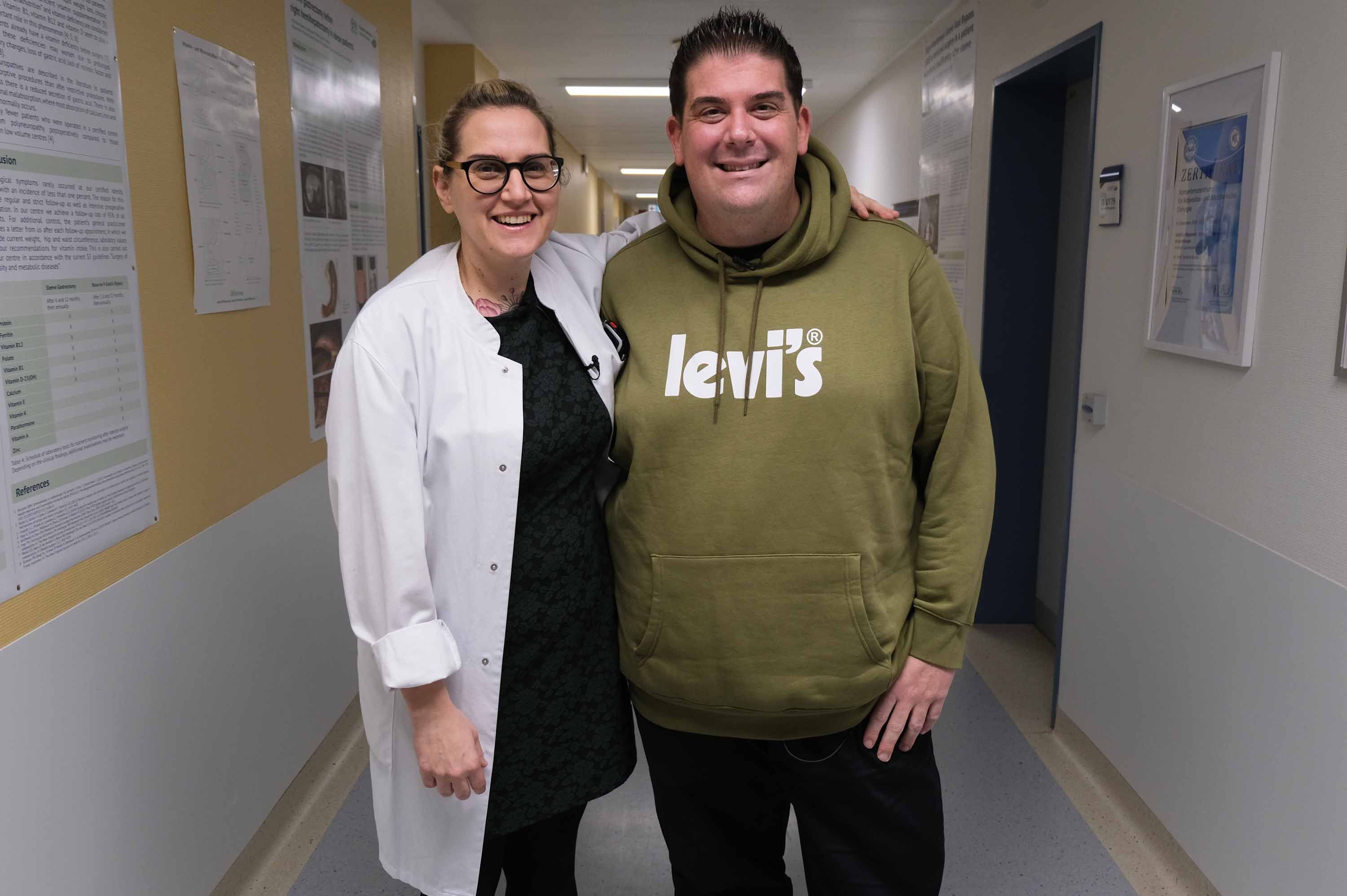 Dr. Jacobi und Daniel Richter stehen auf dem Flur und lächeln in die Kamera