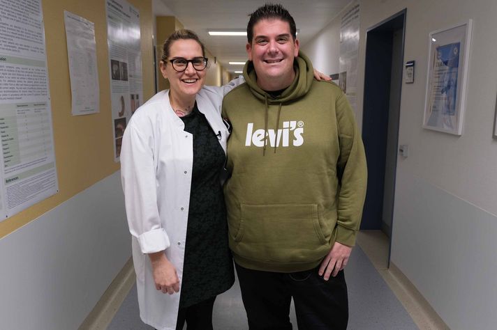 Dr. Jacobi und Daniel Richter stehen auf dem Flur und lächeln in die Kamera