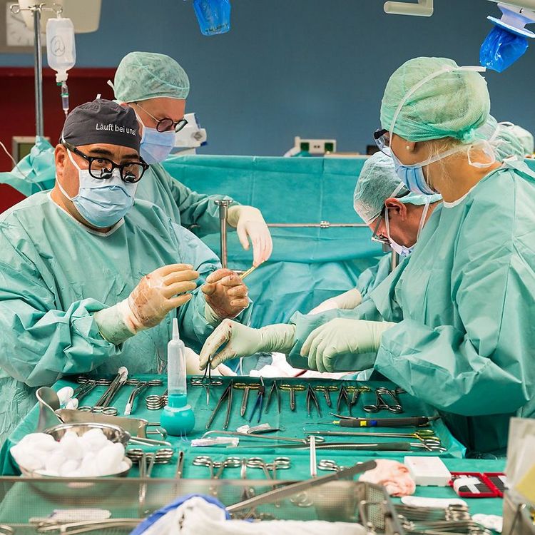 Steriler OP-Saal mit Chirurgieteam bei konzentrierter Arbeit am Operationstisch, mit steriler OP-Kleidung.