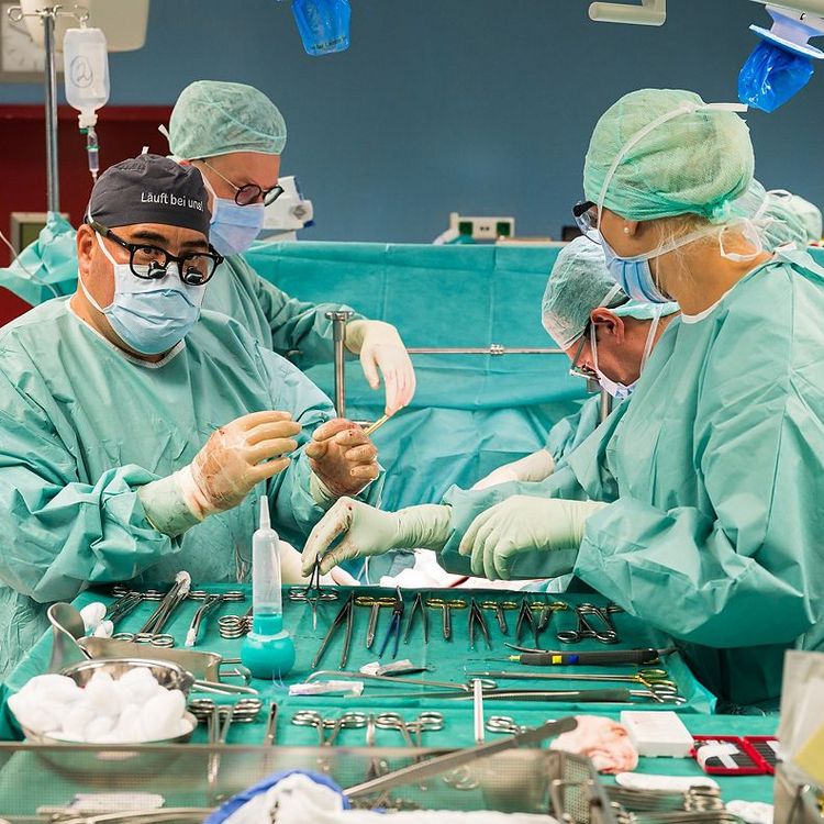 Steriler OP-Saal mit Chirurgieteam bei konzentrierter Arbeit am Operationstisch, mit steriler OP-Kleidung.