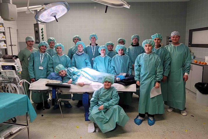 Ein Gruppenfoto in einem Operationssaal. Darauf zu sehen sind 17 junge Männer in blauer OP-Kleidung