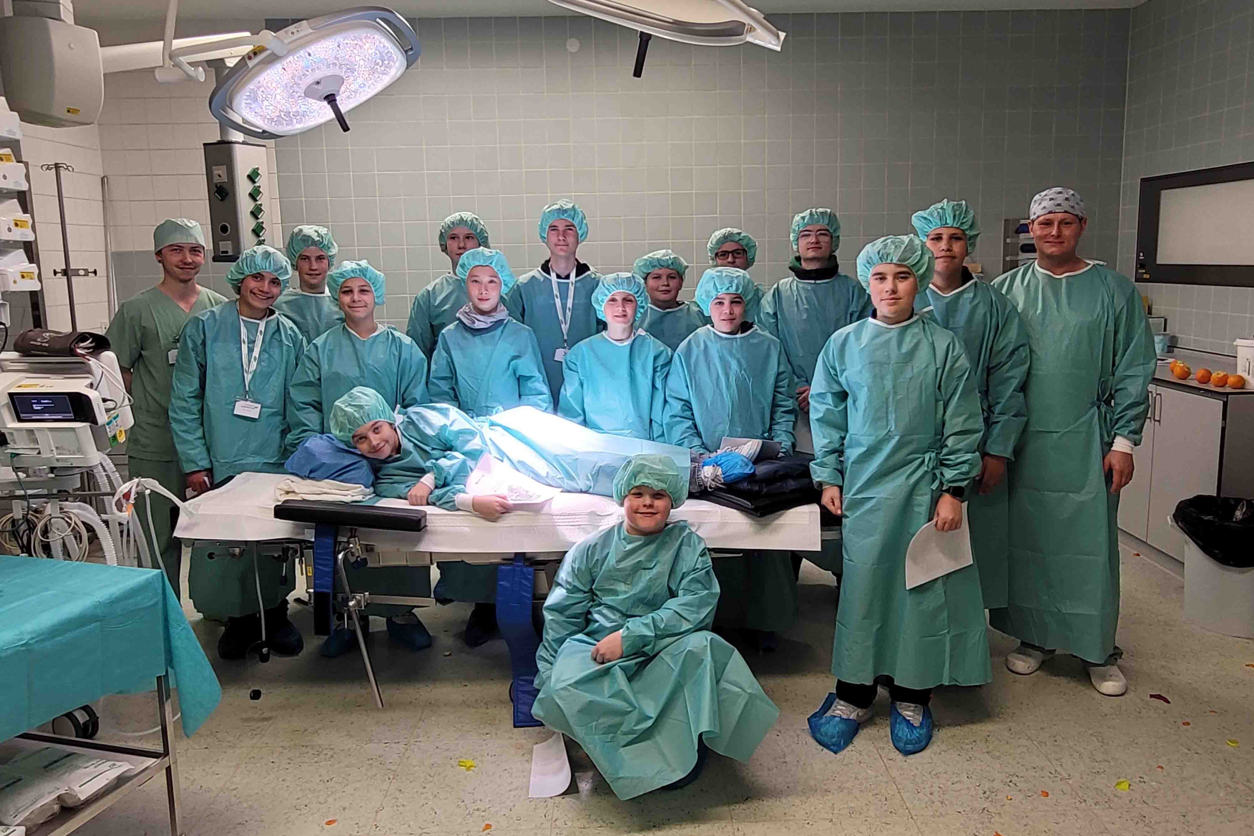 Ein Gruppenfoto in einem Operationssaal. Darauf zu sehen sind 17 junge Männer in blauer OP-Kleidung