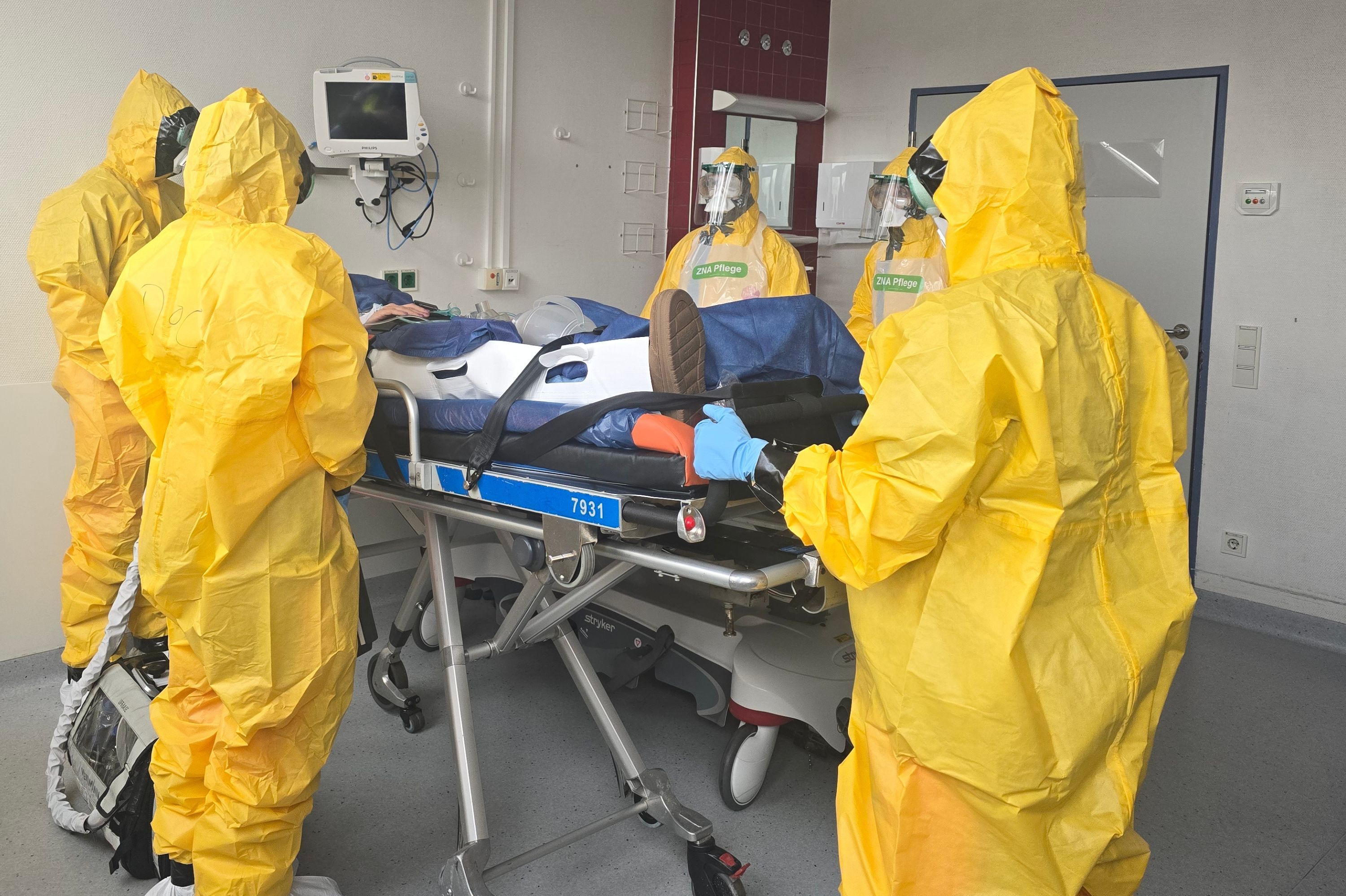 Medizinisches Personal in gelber Schutzkleidung versorgt einen Patienten mit Verdacht auf eine hochansteckende Infektionskrankheit.