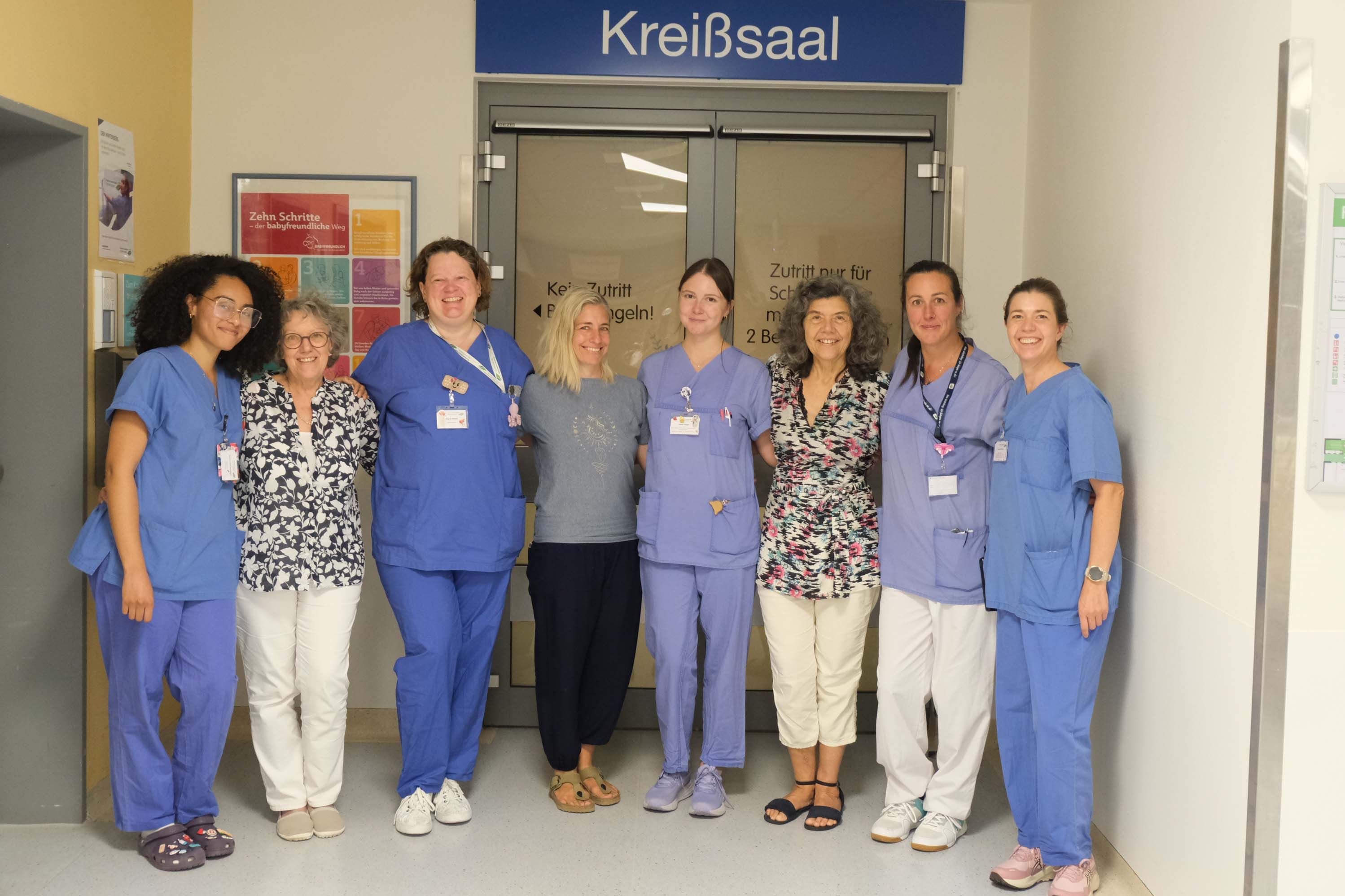 Teamfoto mit mehreren Stillberaterinnen im Klinikum Saarbrücken vor dem Eingang zu Kreißsaal