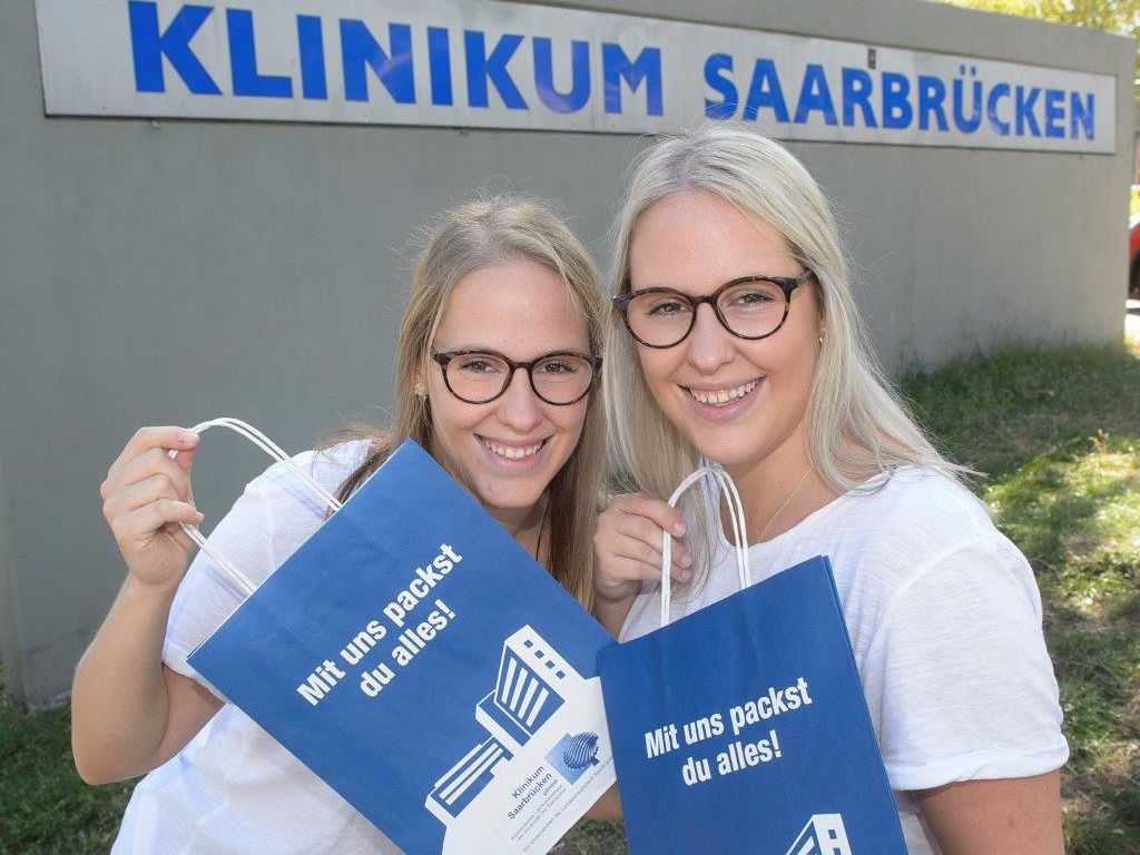 Zwei frühere Azubis mit Taschen des Klinikums Saarbrücken "Mit uns packst Du alles" 
