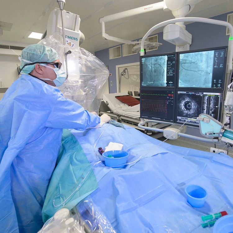 Arzt bei der Behandlung im Herzkatheterlabor in Schutzausrüstung und mit Monitoren