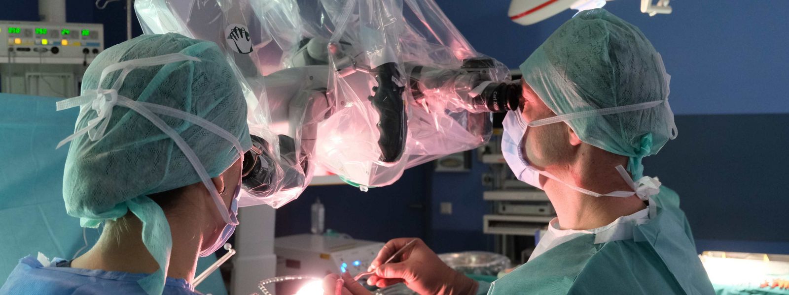 Ein Foto aus einem Operationssaal. Darauf zu sehen sind zwei Ärzte, die gerade operieren und durch eine spezielle OP-Brille gucken Slider_Neurochirurgie.jpg