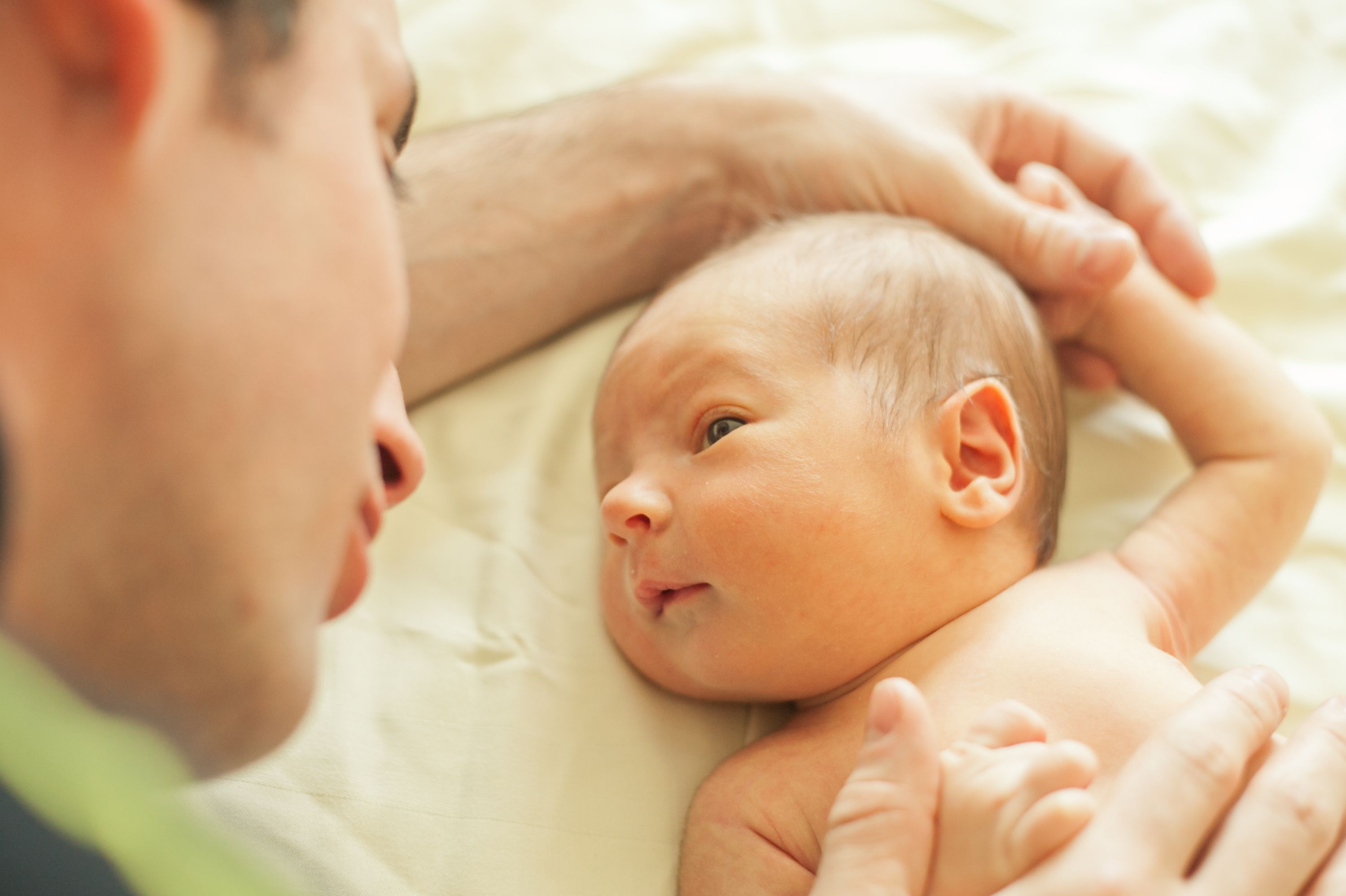 Mann im Profil schaut Neugeborenes an.