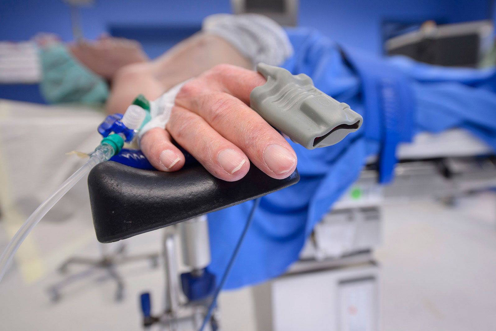 Hand im Operationssaal an die eine Infusion und Pulsmesser angeschlossen sind