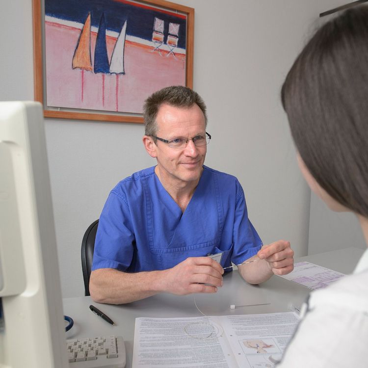 Arzt sitzt gegenüber am Schreibtisch und informiert den Patient 