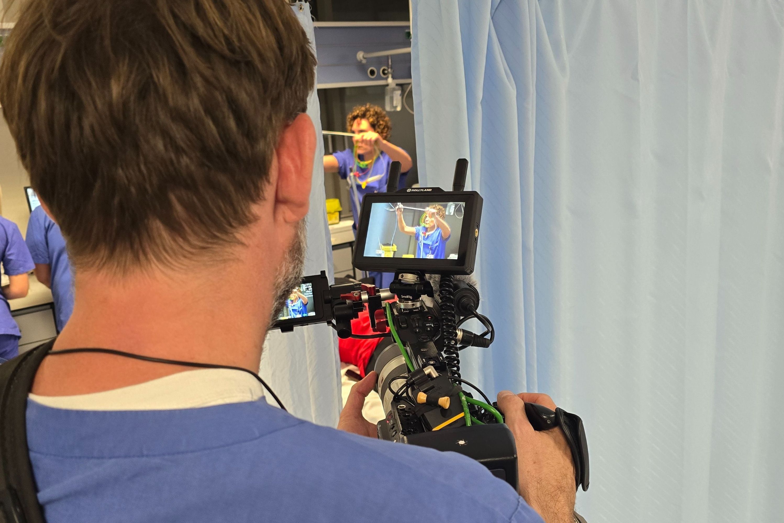 Durch die Kamera sehen wir in eine Behandlungssituation in der Notaufnahme, in der eine Pflegekraft sich um einen Patienten kümmert.