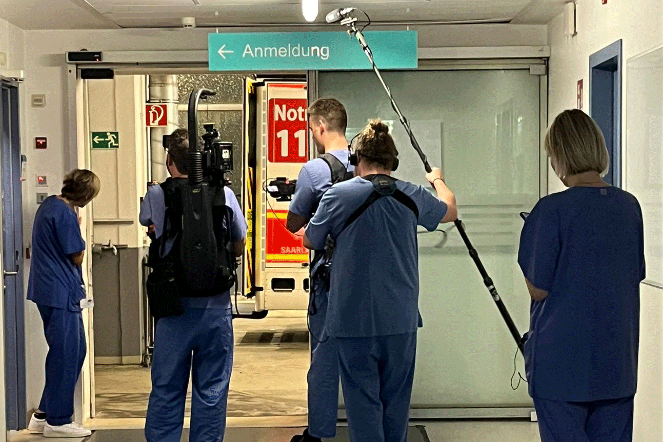 Ein Drehteam steht im Flur der Notaufnahme und wartet auf einen Patienten aus dem Krankenwagen. 