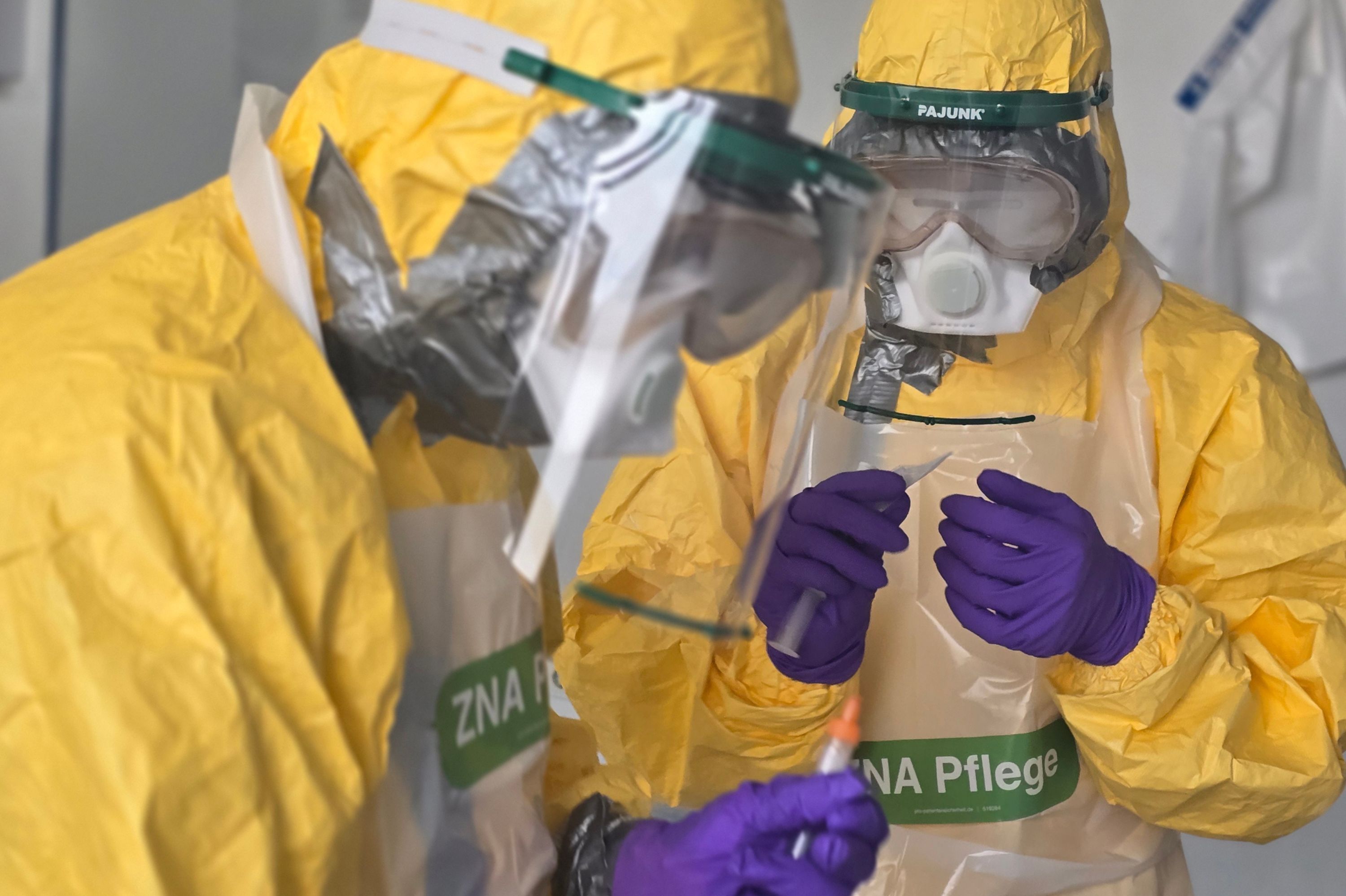 Zwei Pflegekräfte in gelben Infektionsschutzanzügen.