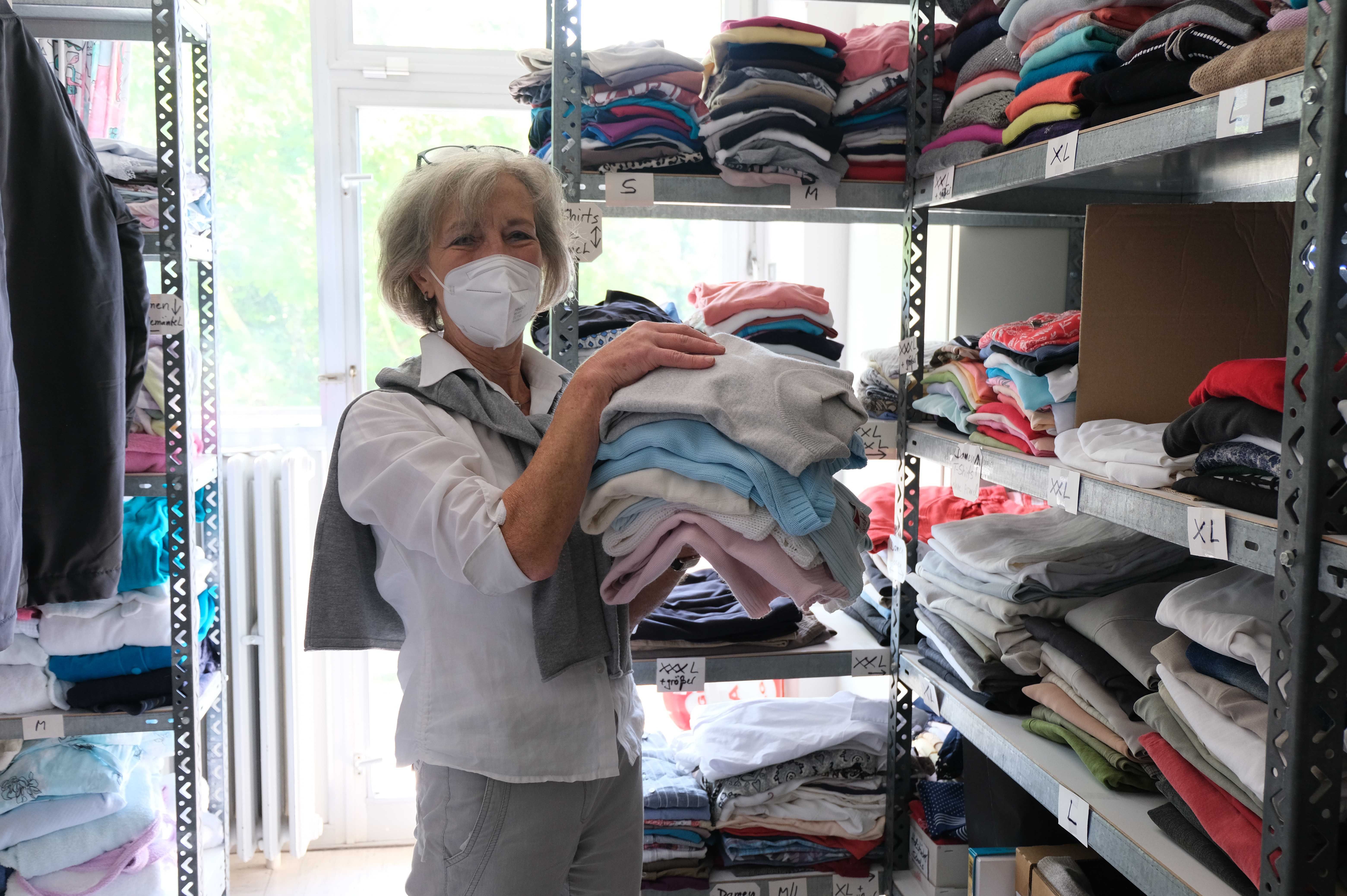 Hanne Wiesener mit einem Stapel Wäsche in der Kleiderkammer vor Regalen.