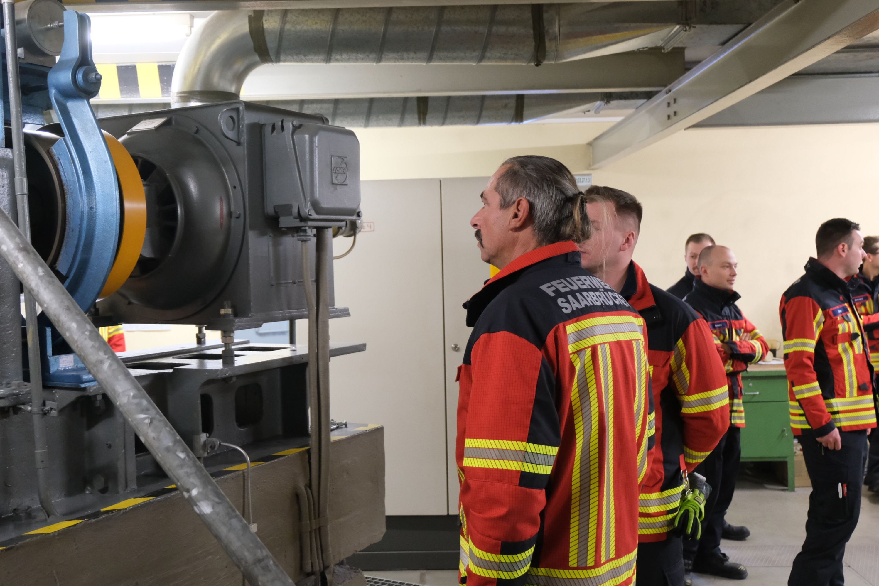 Eine Gruppe aus Feuerwehrleuten schaut sich den Maschinenraum an.