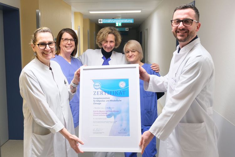 Ein Teamfoto der Mitarbeitenden des Adipositaszentrums. Fünf Personen stehen auf einem hellen Flur und halten einen Rahmen mit der Zertifizierung in die Kamera.