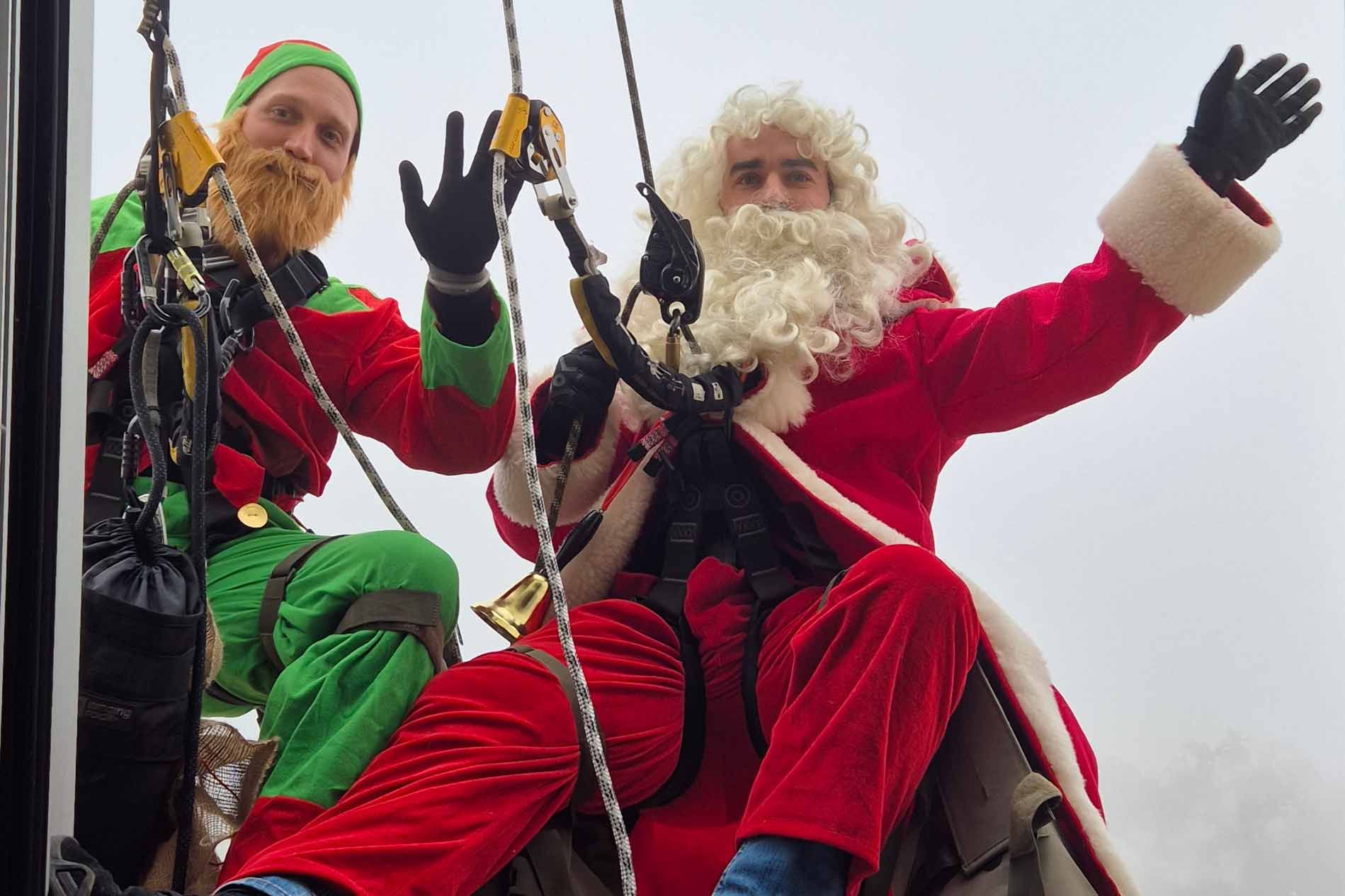 Weihnachtsmann und Wichtel winken in die Kamera.