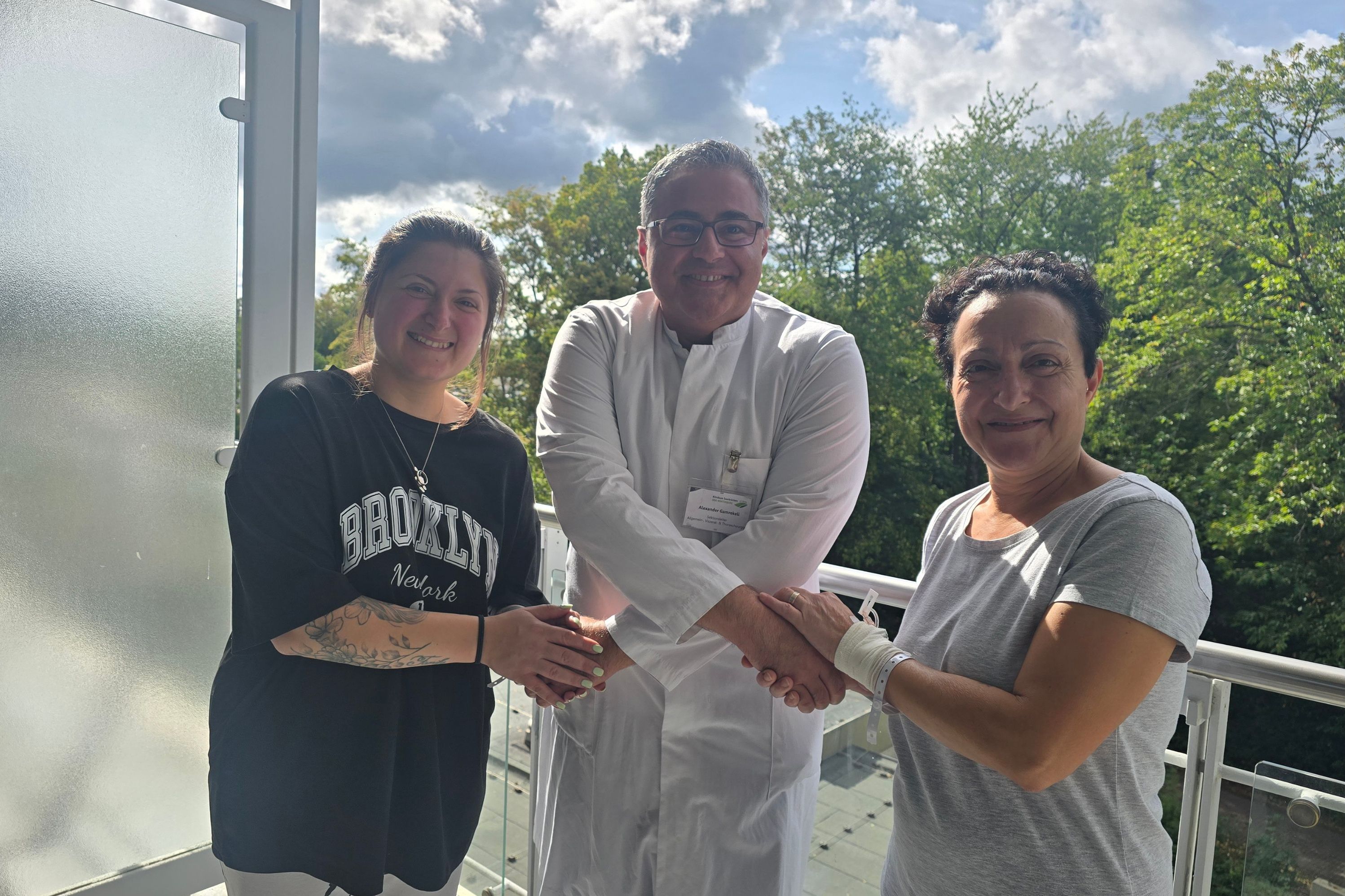 Das Foto zeigt Thoraxchirurg Alexander Gamrekeli, wie er über Kreuz zwei Patientinnen, die rechts und links von ihm stehen, die Hände gibt. Er hat beide operiert, weil sie übermäßig an den Händen geschwitzt haben. Die Zeiten sind jetzt vorbei.