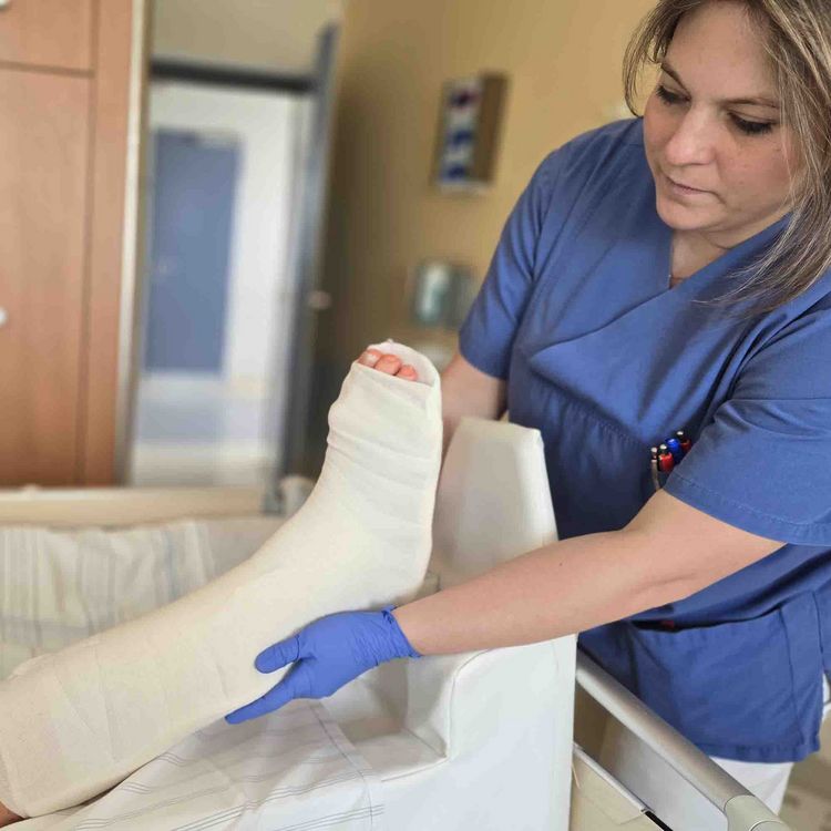 Eine Pflegekraft hebt vorsichtig das Gipsbein einer Patientin an und lagert es neu.