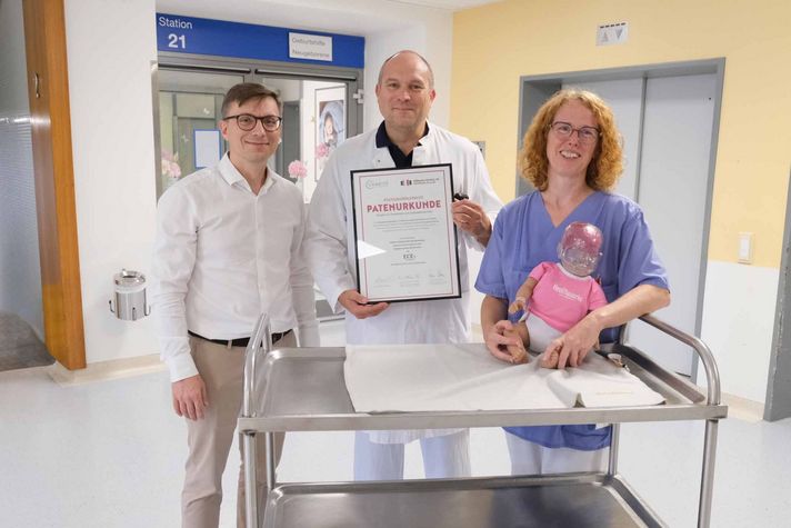 Auf dem Foto sieht man den Chefarzt Dr. Baum, die Stationsleitung Monika Peter und Sergei Vadiaev, der eine Übungspuppe an die beiden anderen überreicht