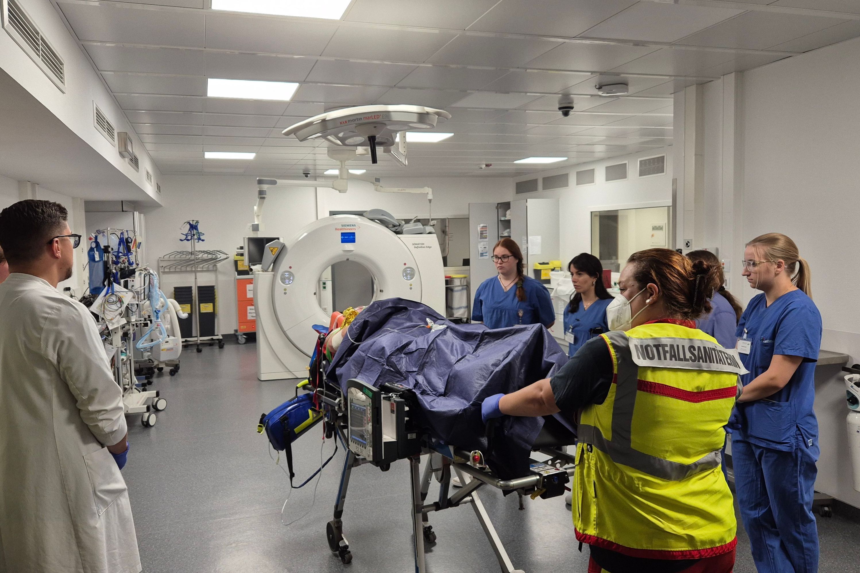 Ein Patient wird auf einer Liege in den Schockraum der Notaufnahme geschoben. Das Ärzte- und Pflegeteam steht schon bereit.