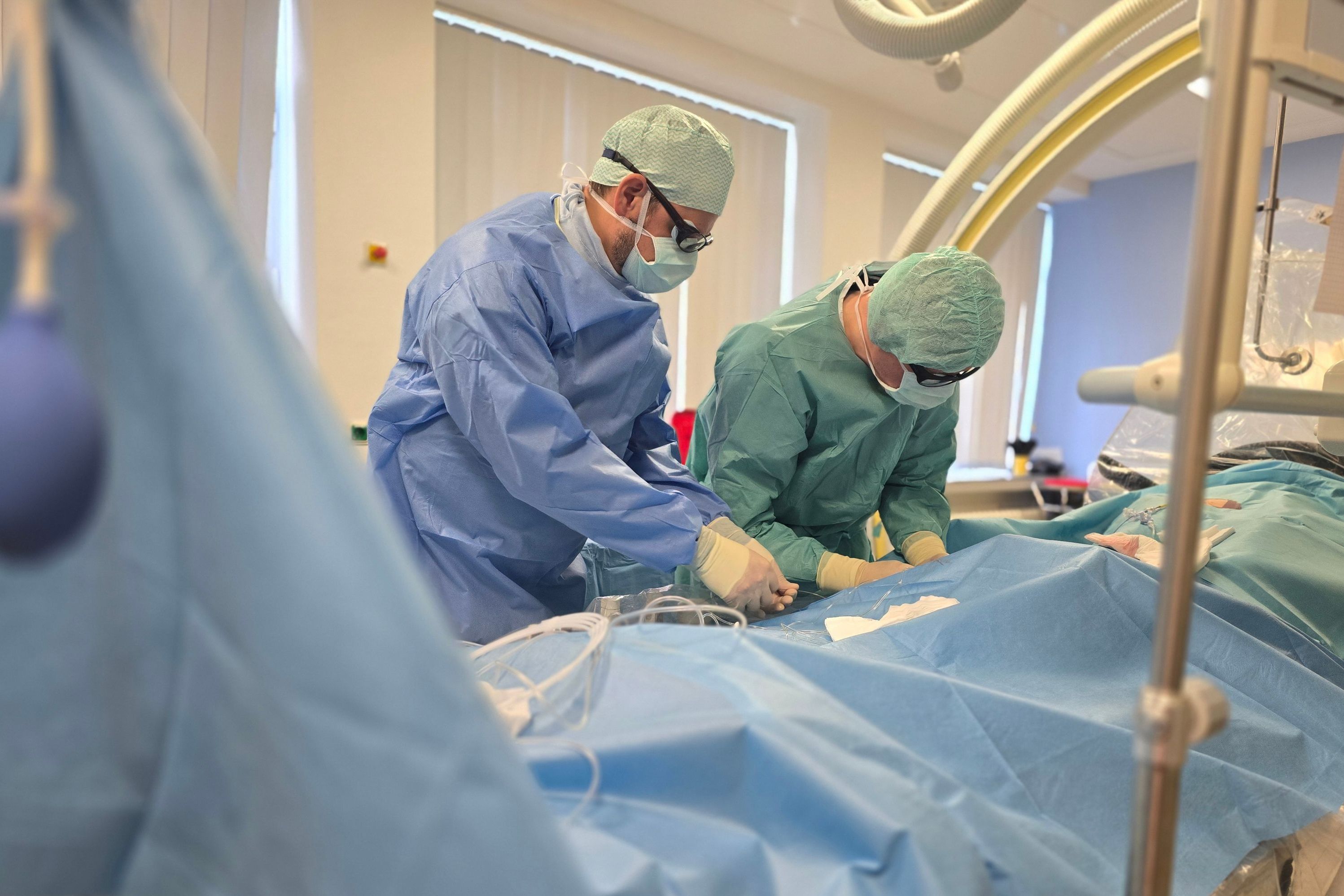 Das Bild zeigt zwei Radiologen bei einem Eingriff, sie sind steril gekleidet und behandeln einen Patienten.