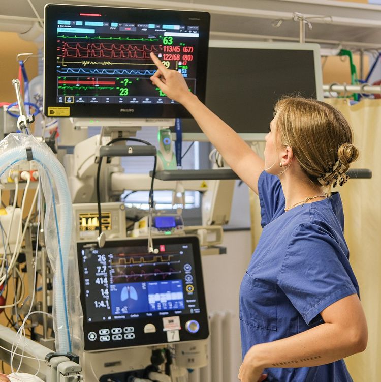 Auf dem Foto sieht man eine Auszubildende, die auf einen Monitor am Patientenbett zeigt