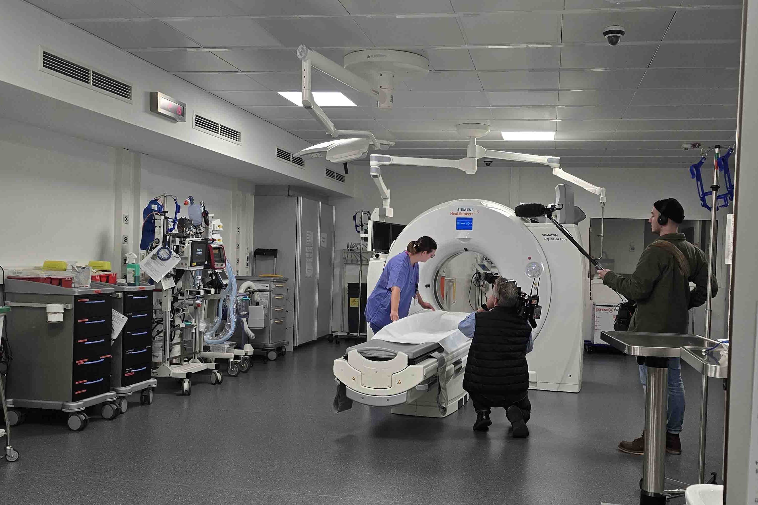 Pflegefachkraft Melanie Braun zeigt dem Kamerateam, wie sie den Schockraum vorbereitet, bevor ein Patient eintrifft. In diesem Fall legt sie gerade eine Unterlage auf der Liegefläche des Computertomographen aus.