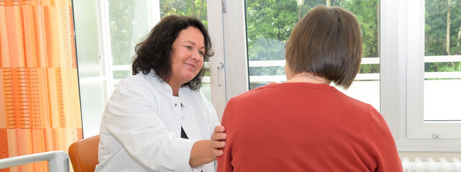 Claudia Bewermeier, Leiterin des Palliativdienstes, legt die Hand auf den Arm einer Patientin, die aus dem Fenster blickt Slider-Palliativ-5.jpg