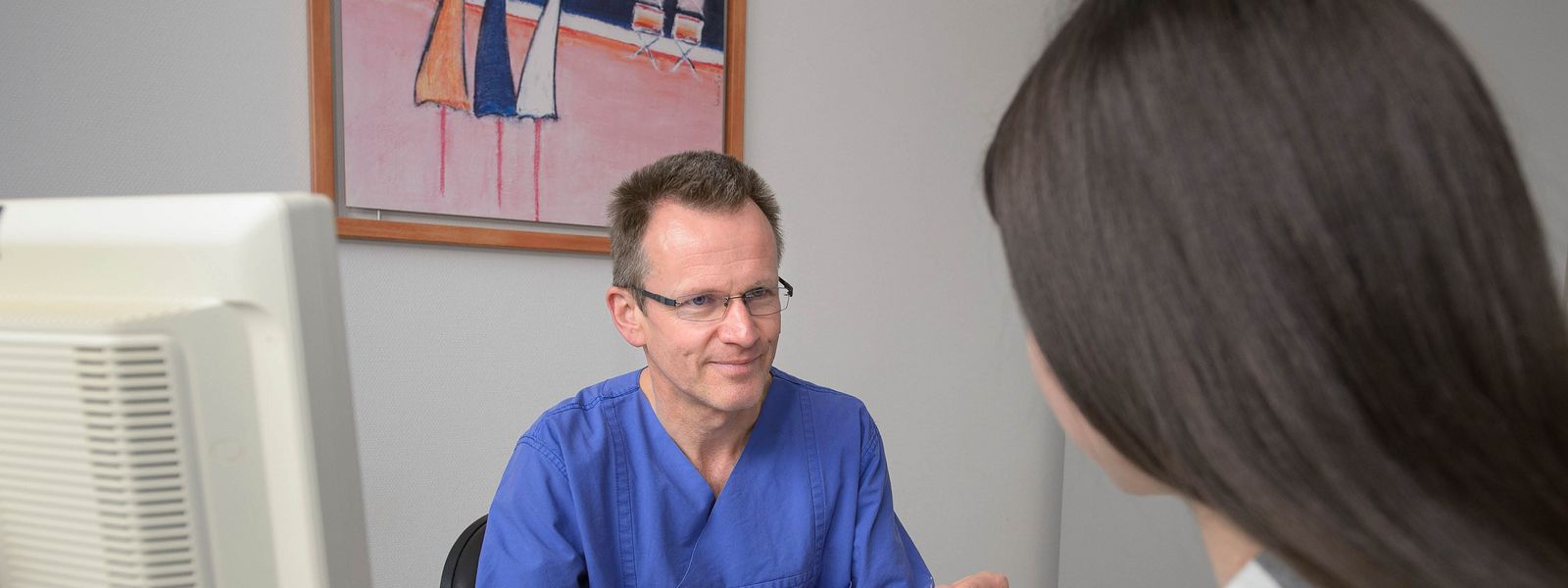 Arzt sitzend am Schreibtisch im Gespräch mit einer Patientin ZIN_Slider_3.jpg