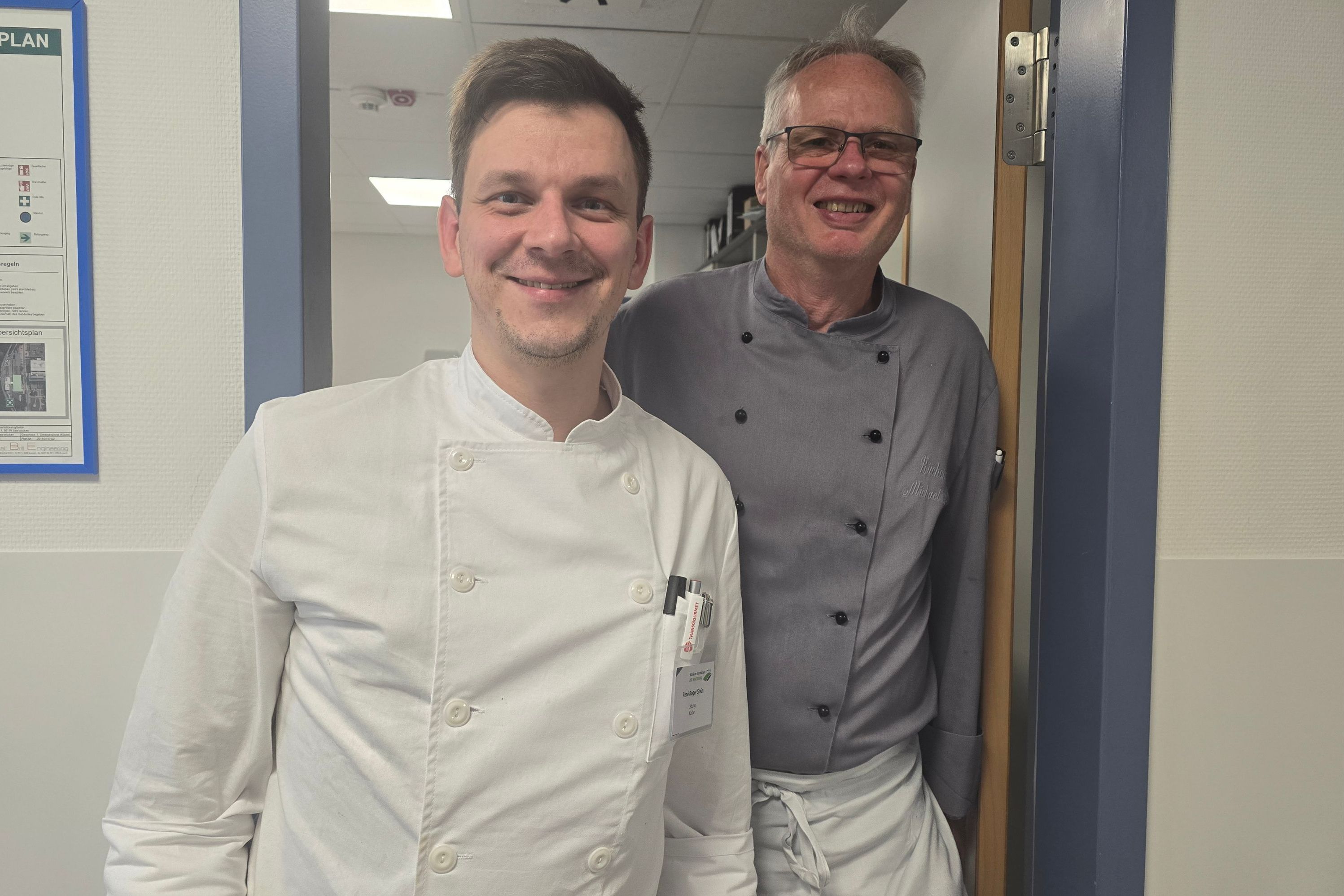 Der neue und der alte Küchenchef stehen nebeneinander und lachen in die Kamera.