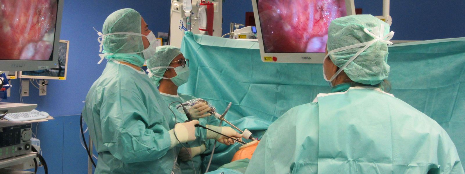 Blick in den Operationssaal, über einen Bildschirm sehen die Operateure und das medizinische Personal beim minimalinvasiven Eingriff, wohin sie ihre Geräte steuern. Der Patient ist hinter einem Tuch verbogen. OP_Gamrekeli_neu.jpg