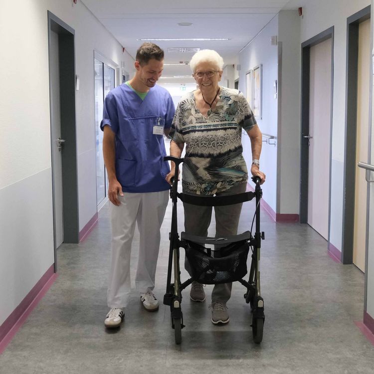 Patientin mit Rollator und Pfleger