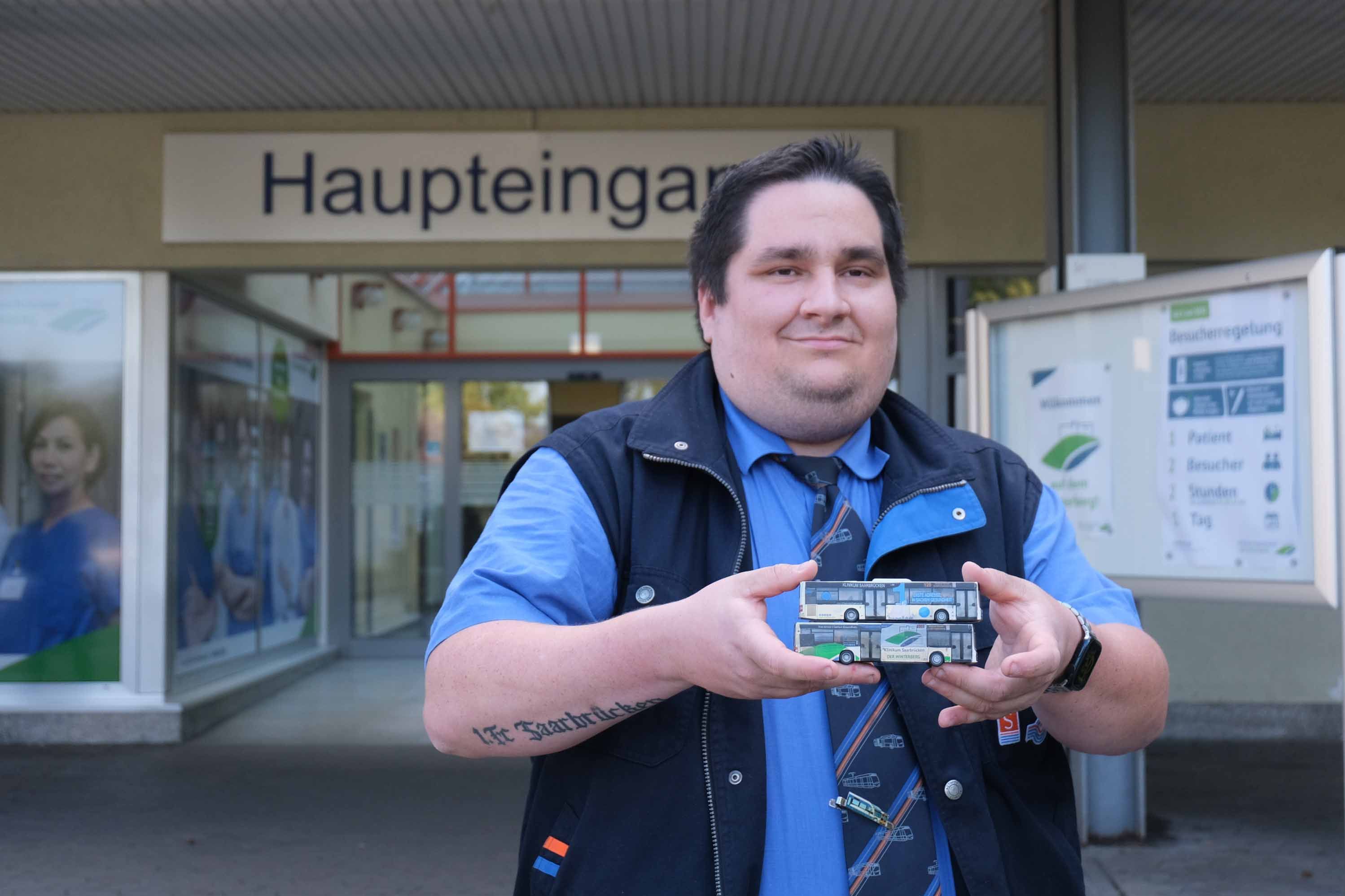 Jan Schwemm zeigt seine Modellbusse vor dem Haupteingang des Klinikums Saarbrücken