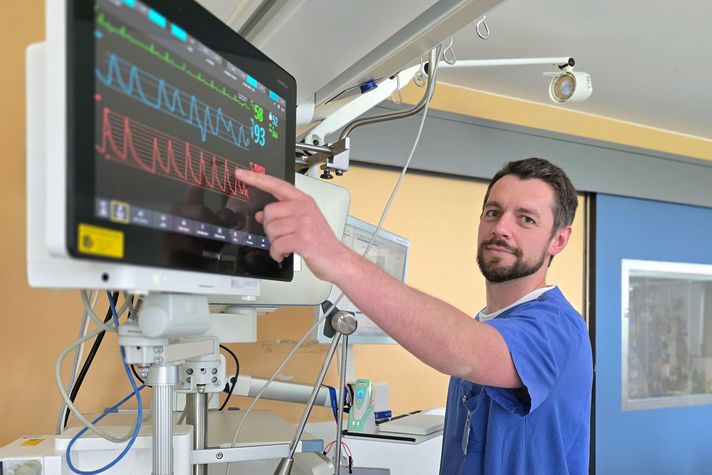 Stationsleitung Karsten Schmitt zeigt auf einen Überwachungsmonitor am Patientenbett.