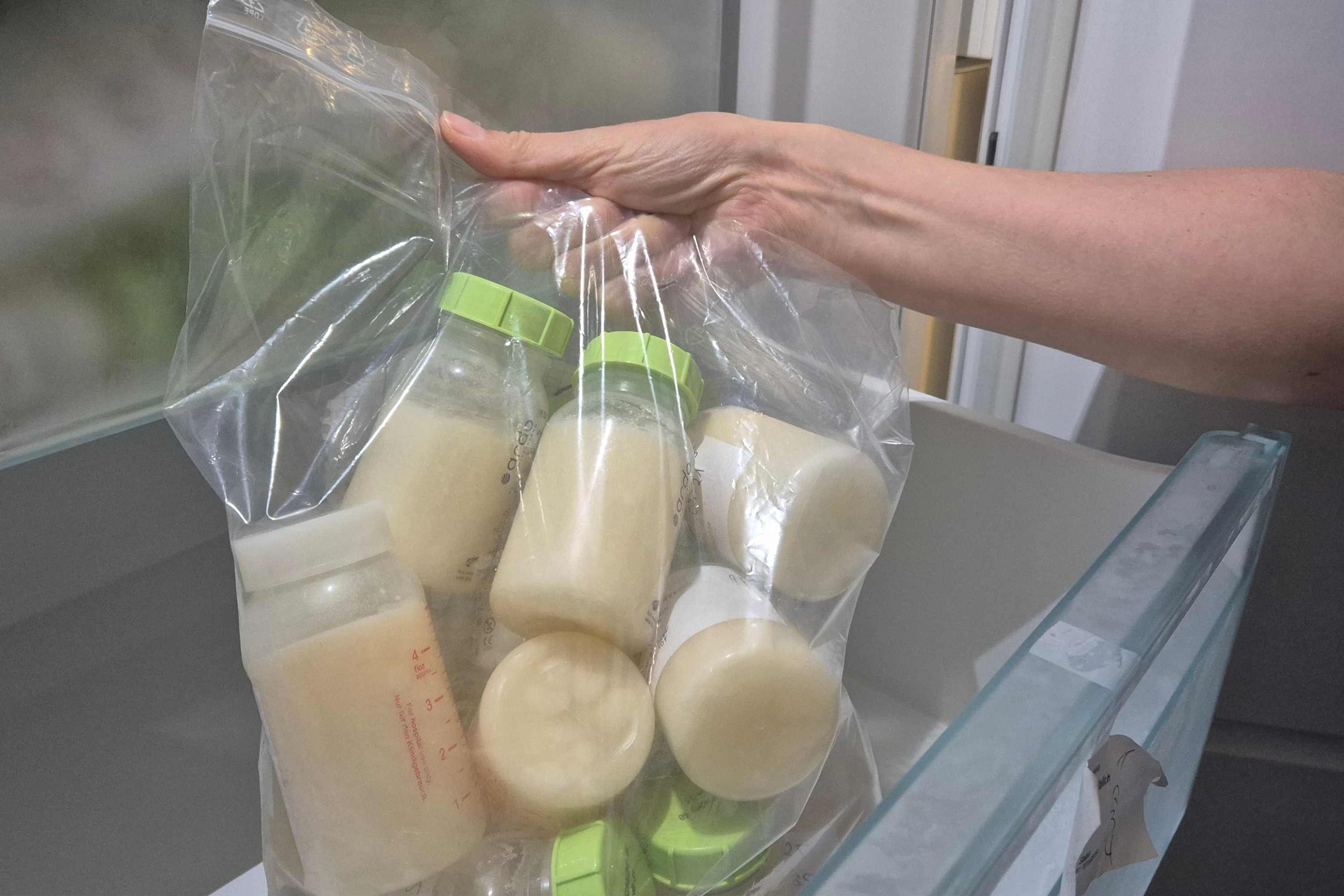 Hand hält eine Tüte mit Fläschen, die Frauenmilch enthalten