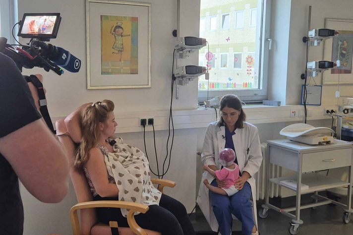 Dr. Claire-Detemple hält eine Schüttelpuppe in der Hand und spricht mit einer Mutter