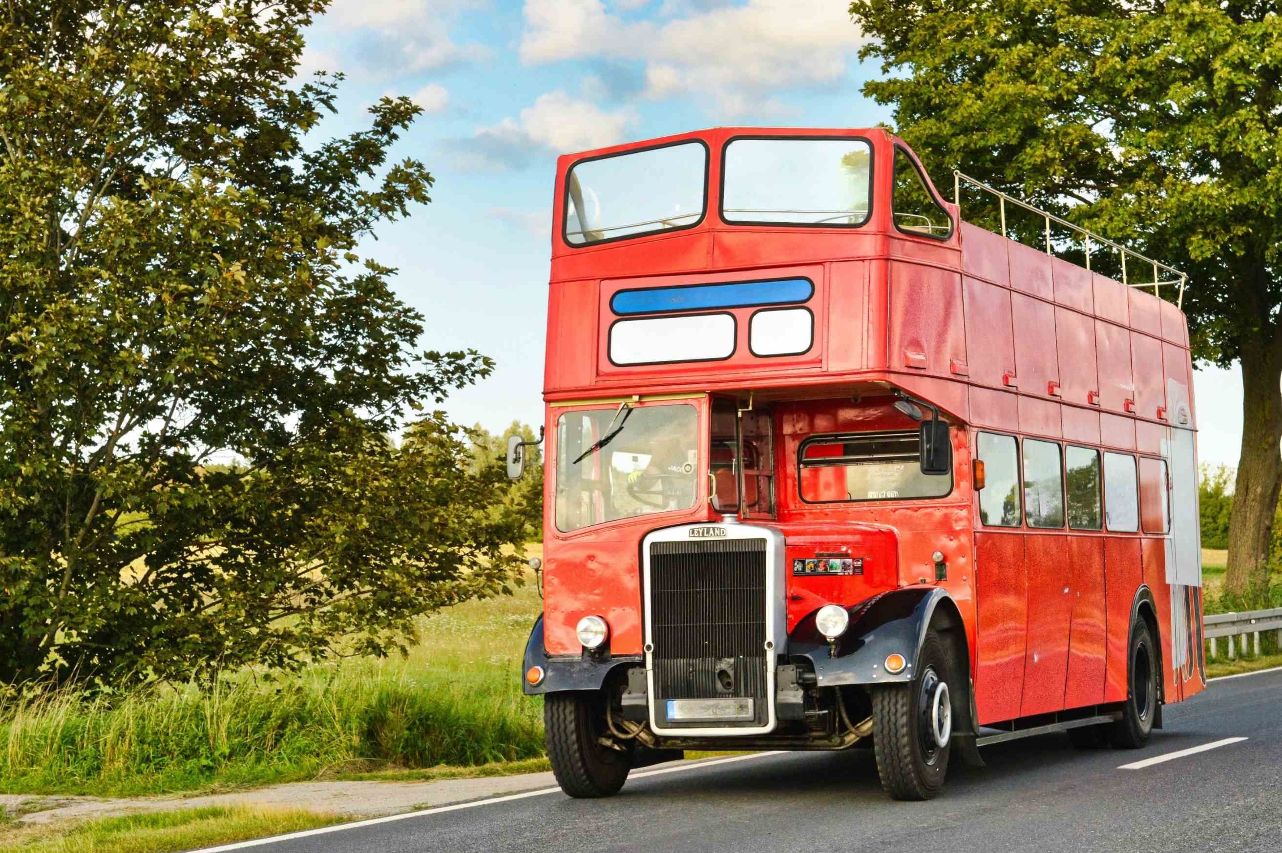Roter Doppeldeckerbus auf einer Landstraße. 