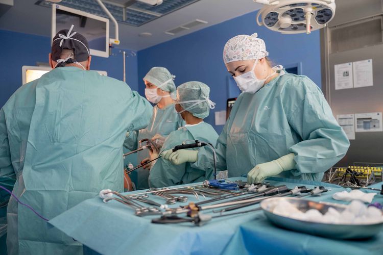 Blick in den OP-Saal während einer Operation, im Vordergrund greift eine Operationstechnische Assistentin nach dem OP-Besteck vom Besteck-Tisch