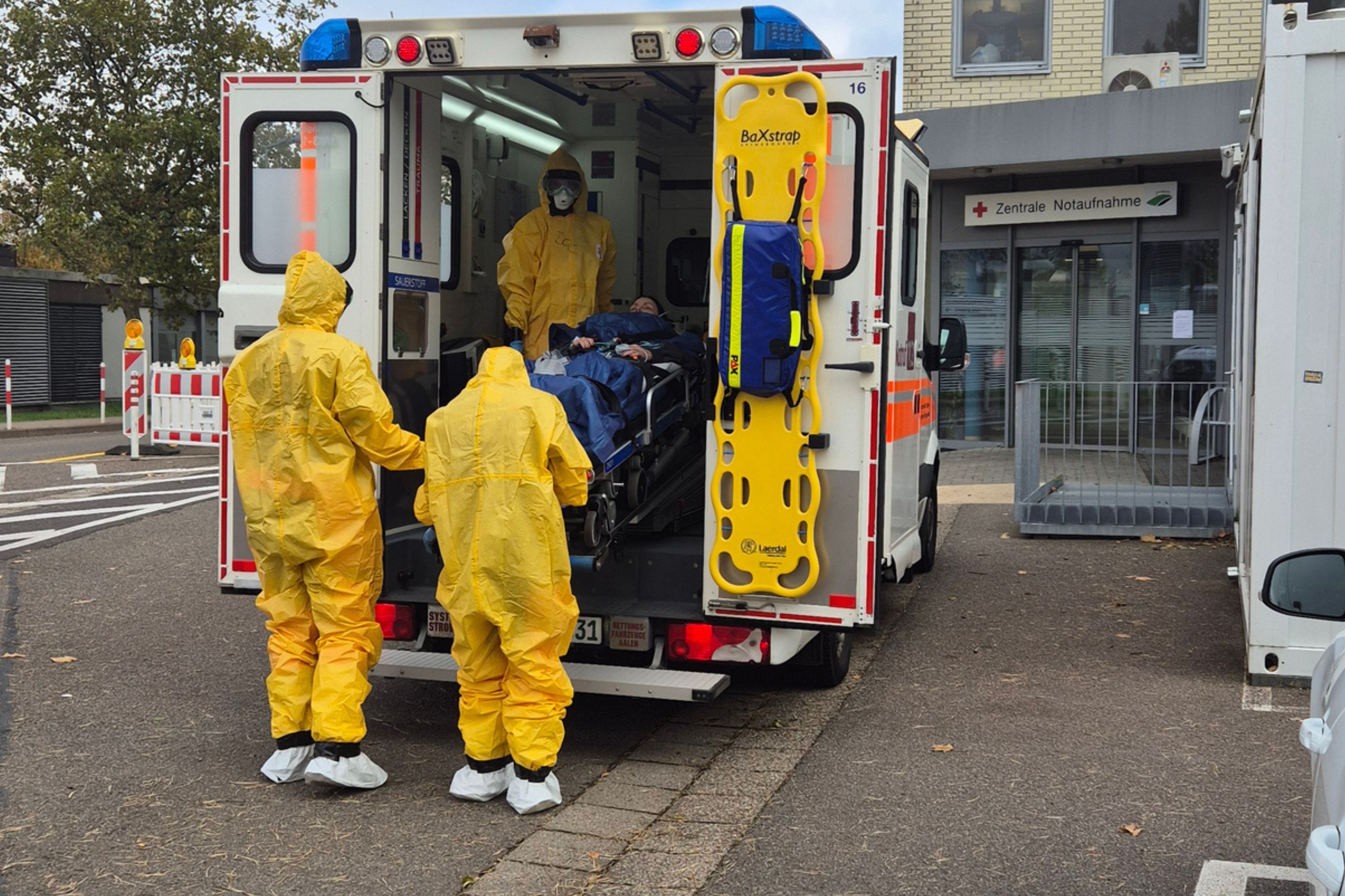 Medizinisches Personal in gelben Schutzanzügen laden einen Patienten aus dem Rettungswagen aus.